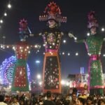 दशहरा मेले में रोशनी के बीच खड़े रावण और अन्य विशाल पुतले, आसपास मौजूद श्रद्धालु और दर्शक
