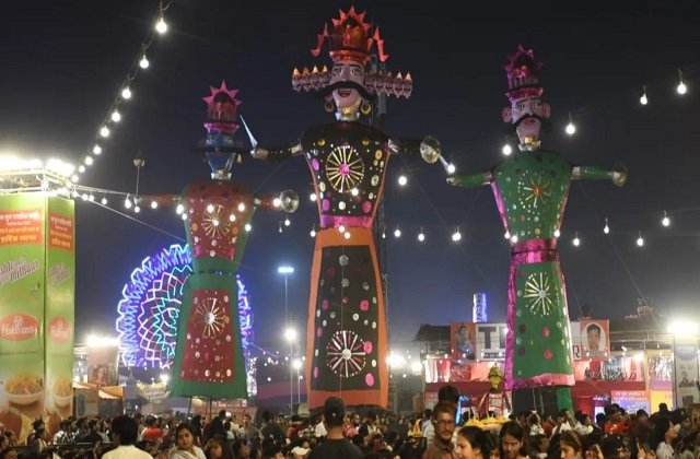 दशहरा मेले में रोशनी के बीच खड़े रावण और अन्य विशाल पुतले, आसपास मौजूद श्रद्धालु और दर्शक
